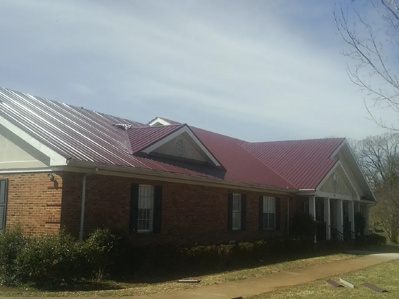 Red metal roof with gabled entries on a long brick building, from a Hail Damage Roof Repair job in Oxon Hill