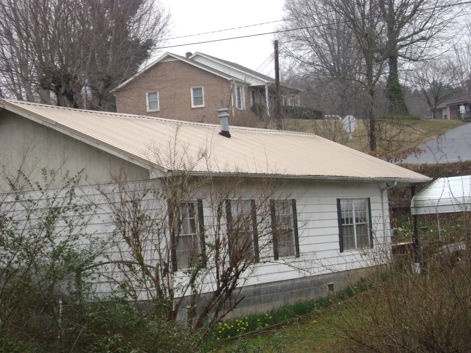 Tan metal roof on a white sided house set into a hillside — Commercial Roofing by Roofing Brothers in Oxon Hill